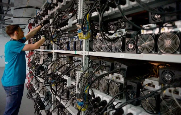 Tecnico al lavoro tra i rack di miner ASIC in una farm di mining Bitcoin